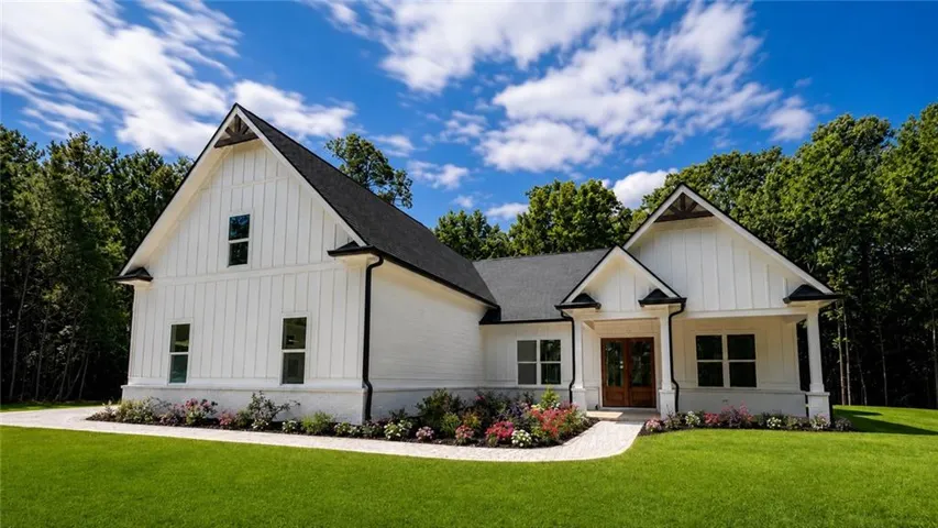 Modern farmhouse exterior featuring white board and batten siding, dark shingle roofing, and a prominent front entry with double wood doors
