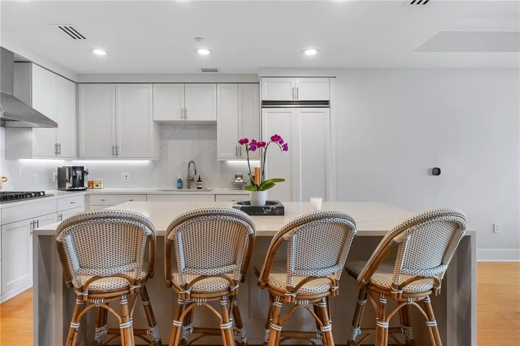 Kitchen with light wood finished floors, white cabinets, wall chimney exhaust hood, a kitchen breakfast bar, and recessed lighting