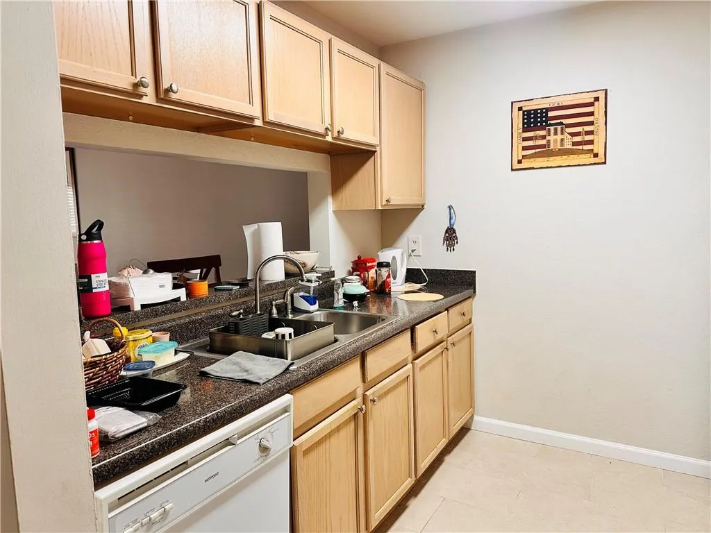 Kitchen featuring dark countertops, light brown cabinets, dishwasher, and light tile patterned floors