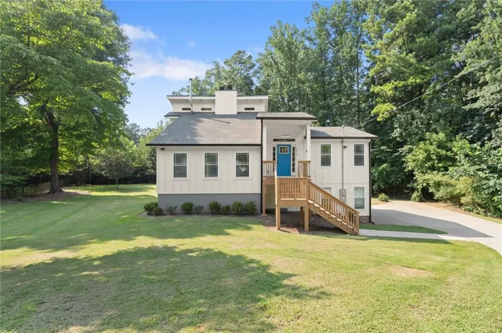 Contemporary residence featuring white board and batten siding, a prominent blue entry door, and a dark shingle roof
