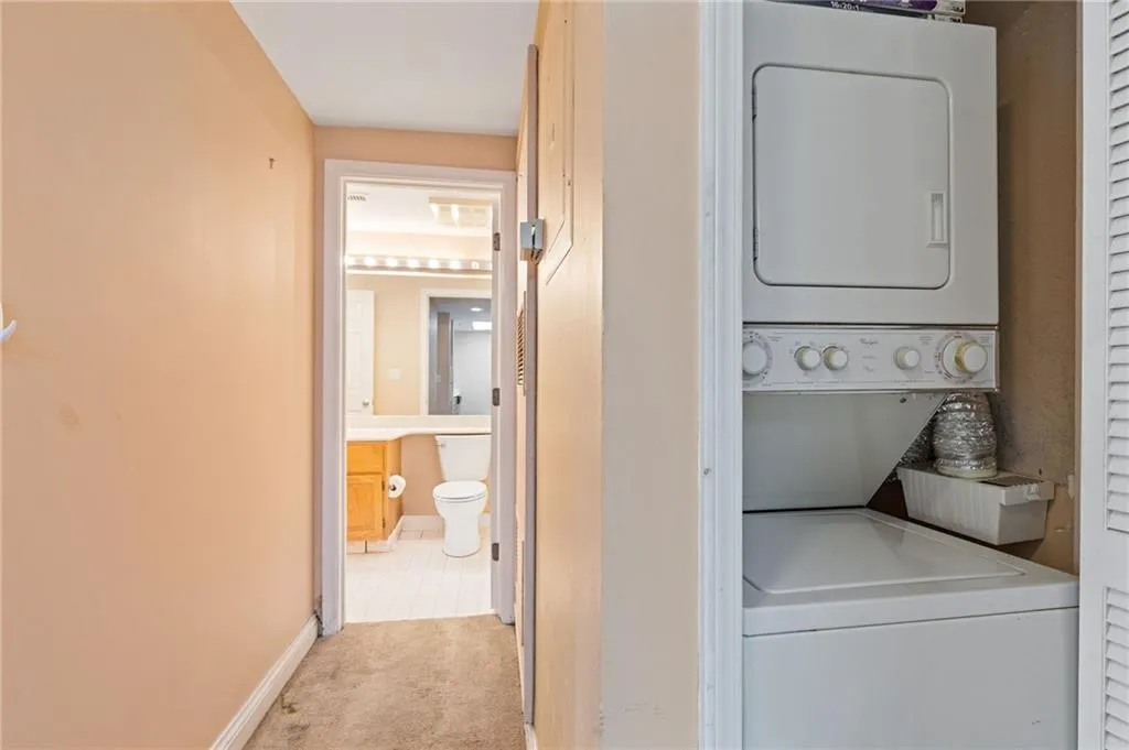 Laundry room with stacked washer and clothes dryer and light carpet
