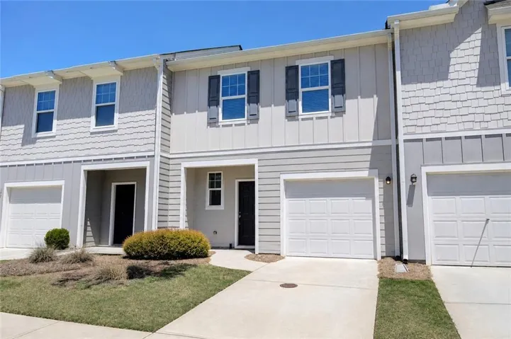 Modern townhome exterior featuring light gray siding, dark window shutters, and a single-car garage