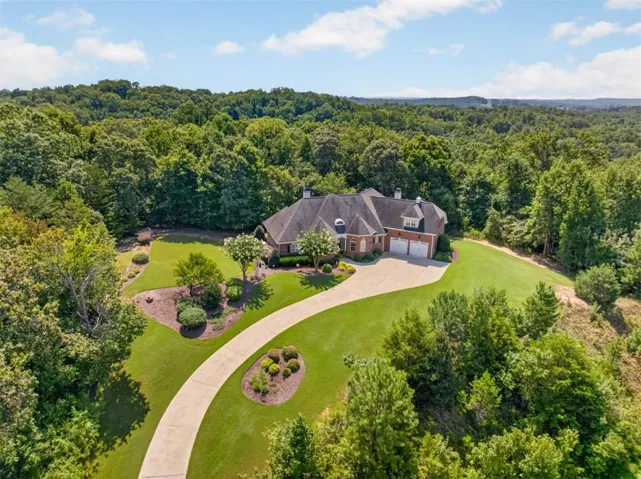 Brick exterior residence with a multi-car garage, expansive driveway, and manicured landscaping, surrounded by mature trees