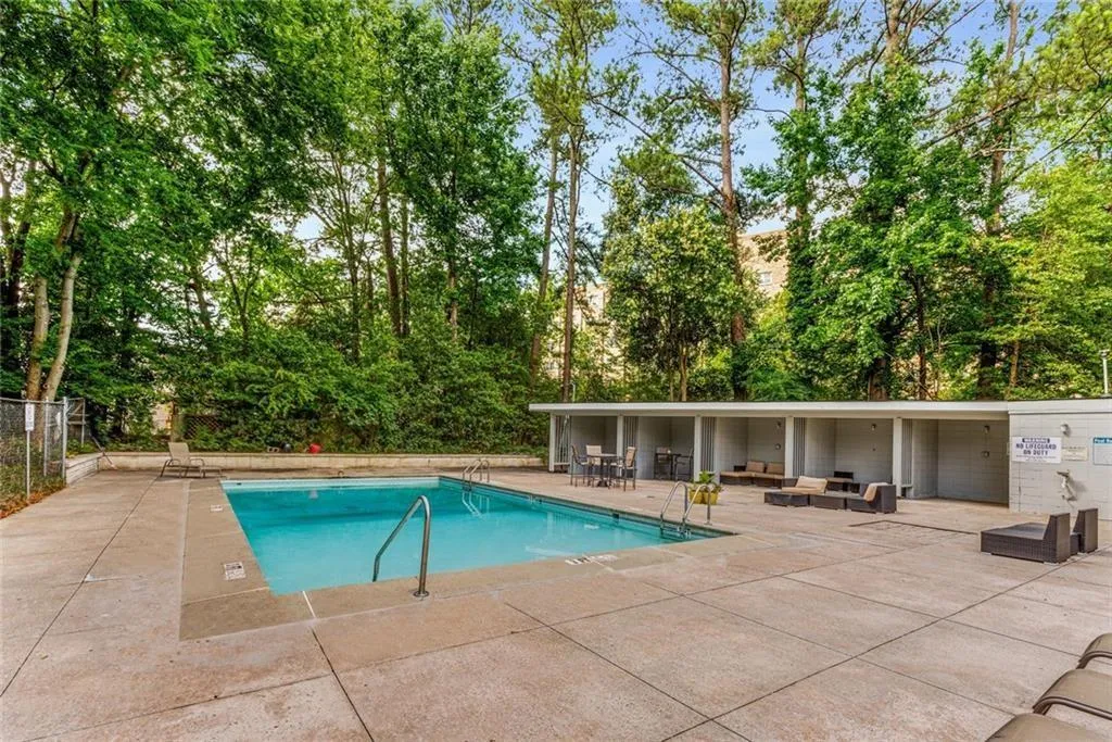 Community pool with a patio area, an outdoor hangout area, and view of wooded area Community pool with a patio area, an outdoor hangout area, and view of wooded area