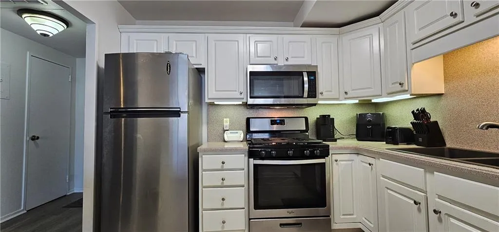 Kitchen featuring stainless steel appliances, white cabinets, light countertops, and dark wood-type flooring Kitchen featuring stainless steel appliances, white cabinets, light countertops, and dark wood-type flooring