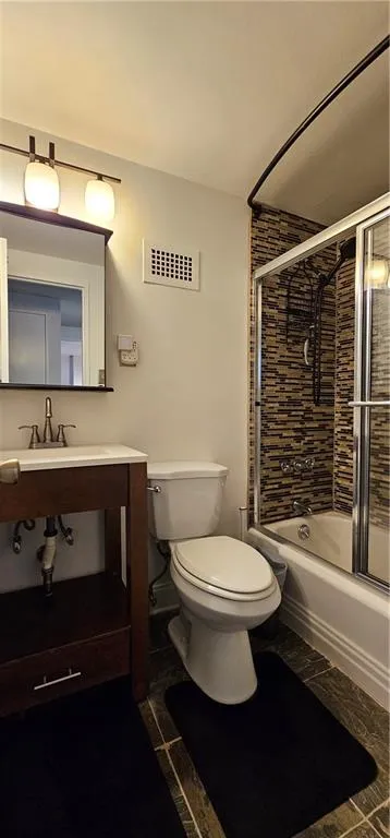 Bathroom with bath / shower combo with glass door, vanity, and dark marble finish flooring Bathroom with bath / shower combo with glass door, vanity, and dark marble finish flooring