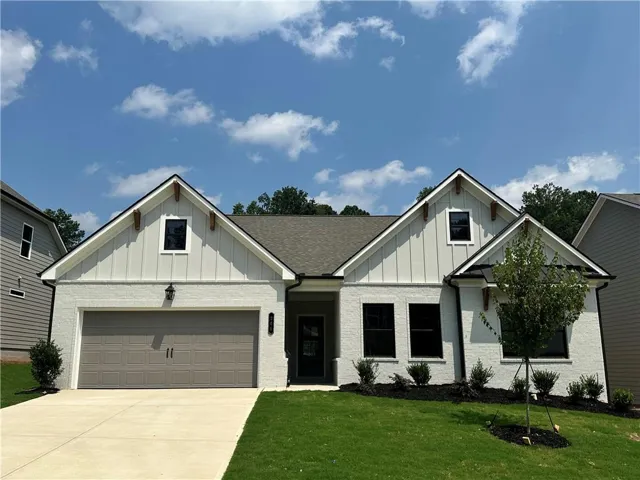 Exterior featuring white painted brick, board-and-batten gables with decorative wood brackets, a gray shingle roof, a two-car garage, and dark-framed windows
