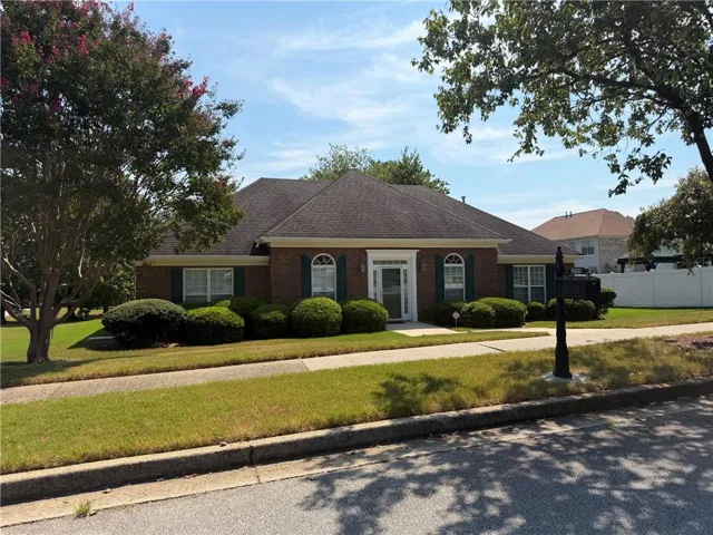 Brick exterior home with a dark shingle roof, arched transom window, shuttered windows, and mature landscaping