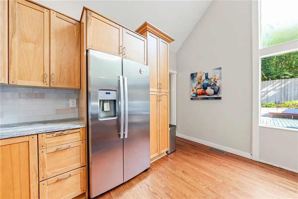 Kitchen featuring stainless steel fridge with ice dispenser, light brown cabinetry, healthy amount of natural light, and high vaulted ceiling