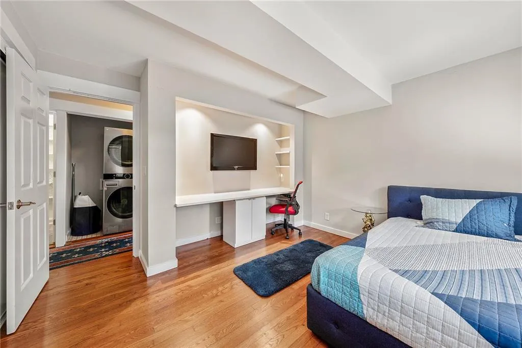 Bedroom with stacked washer / drying machine, built in study area, and wood finished floors