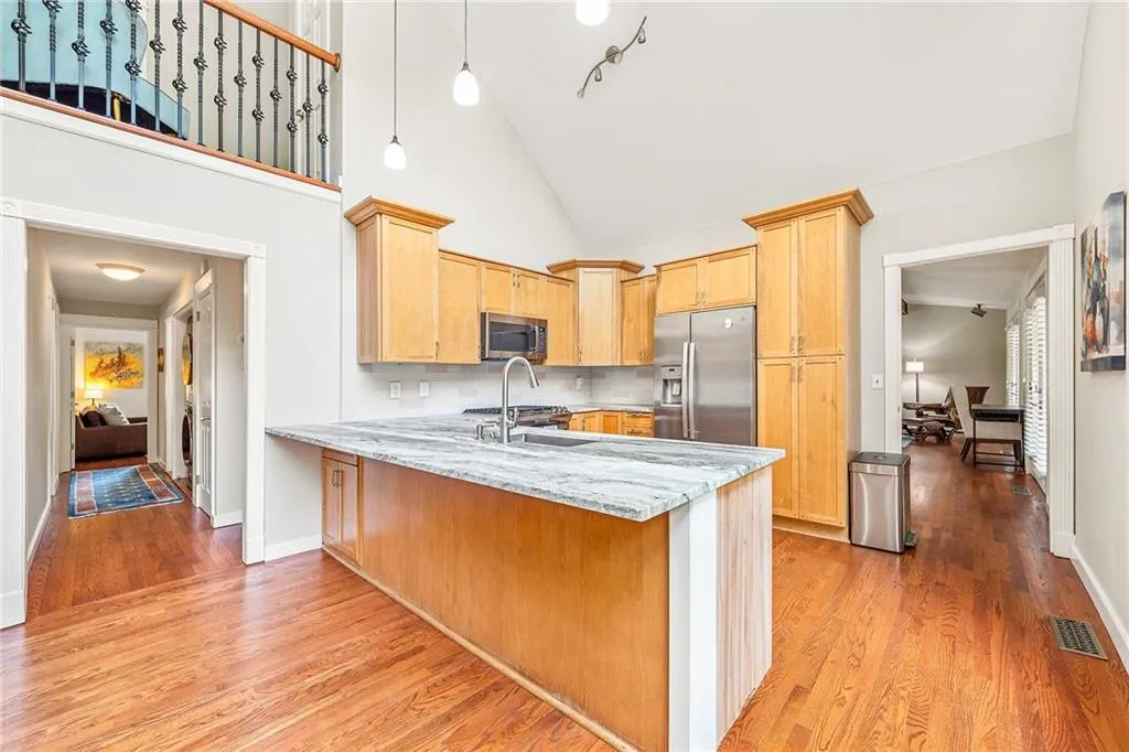 Kitchen featuring a peninsula, stainless steel appliances, decorative backsplash, light wood-type flooring, and high vaulted ceiling