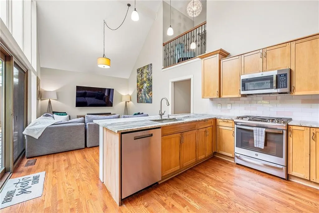 Kitchen with stainless steel appliances, high vaulted ceiling, backsplash, a peninsula, and light wood-type flooring