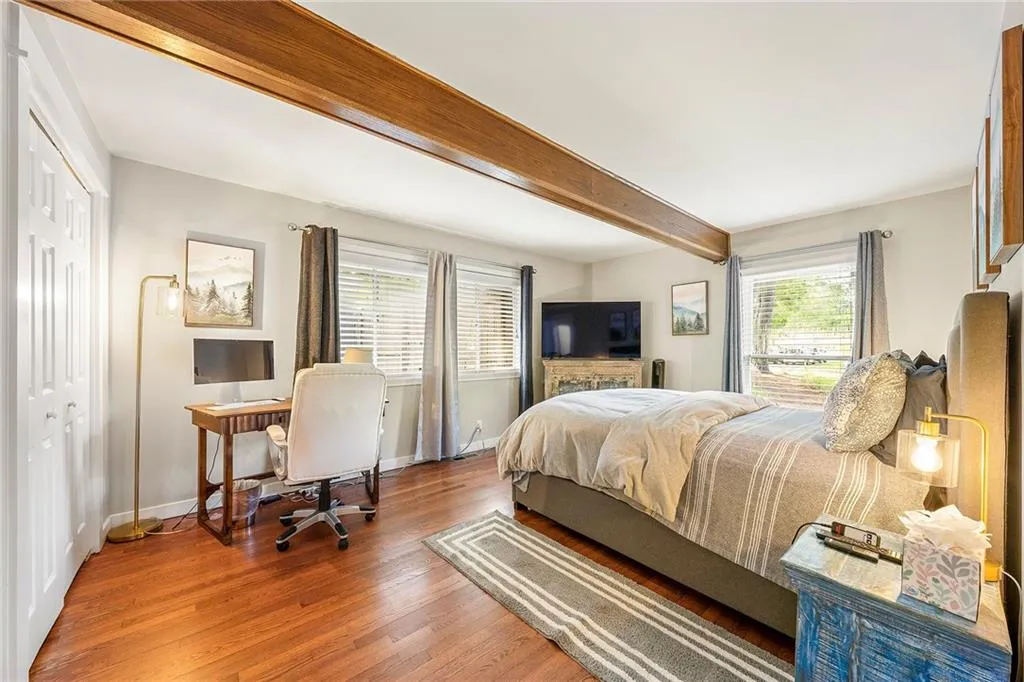 Bedroom featuring beam ceiling, wood finished floors, an office area, and a closet
