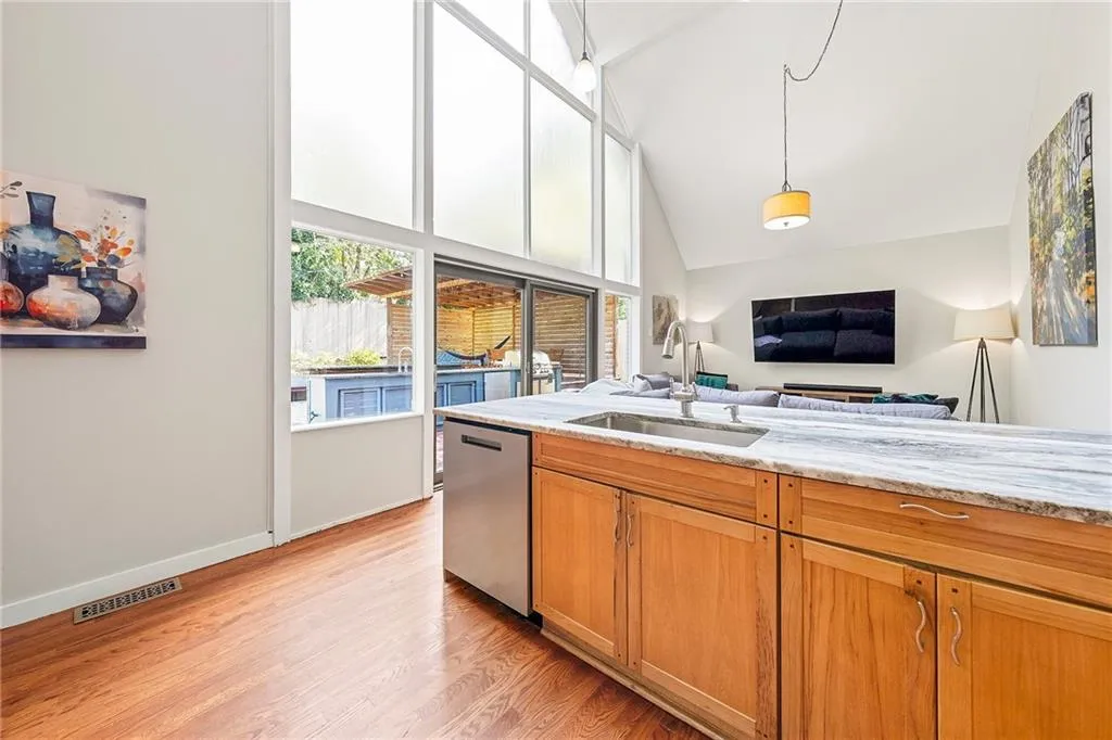 Kitchen featuring light wood-style floors, dishwasher, hanging light fixtures, light stone countertops, and high vaulted ceiling