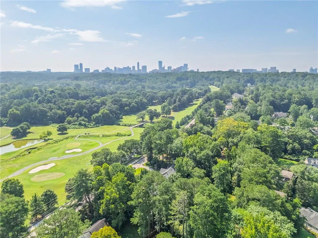 Drone / aerial view of a golf course, a nearby body of water, and city skyline