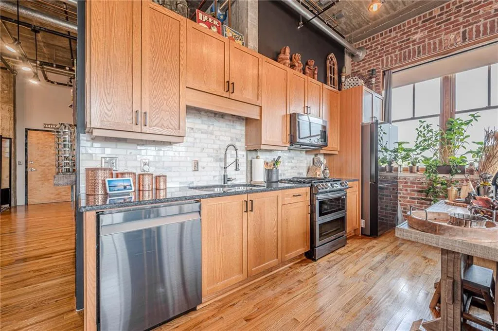 Kitchen featuring wood-finish cabinetry, granite-style countertops, stainless steel appliances, and a subway tile backsplash