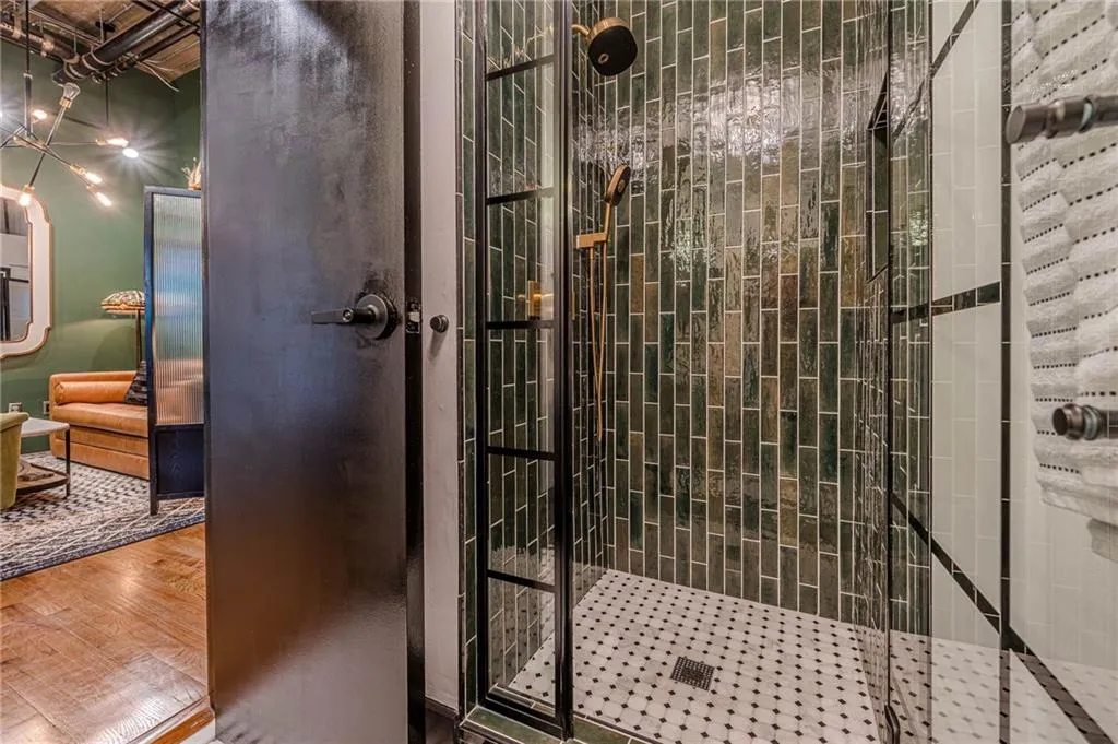 Shower enclosure featuring dark green subway tile, a brass-toned shower head and handheld sprayer, and a black-framed glass door