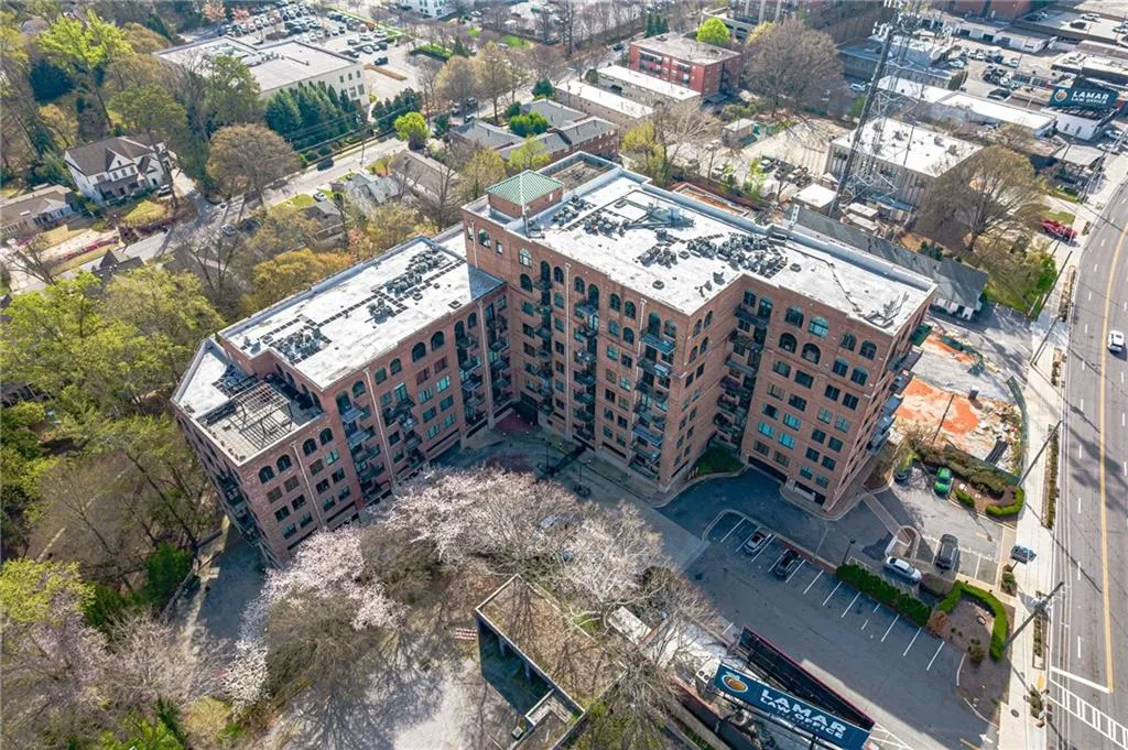 Multi-story brick building featuring arched windows, balconies, and a paved parking area