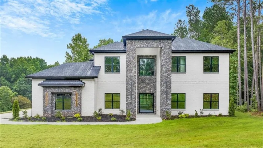 Modern architectural facade featuring white brick, stone veneer accents, multiple large windows, a dark roof, and a meticulously landscaped foreground