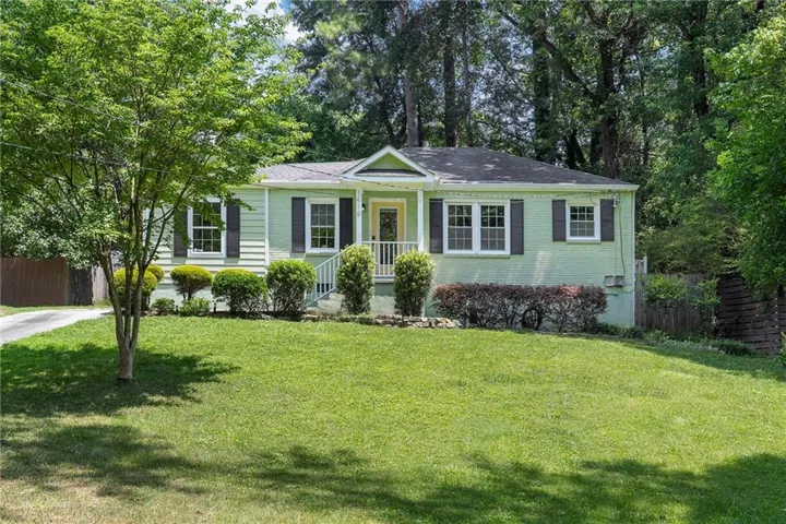 Charming ranch-style home featuring a light-colored exterior with dark shutters, a covered front porch with classical columns, and multiple front-facing windows