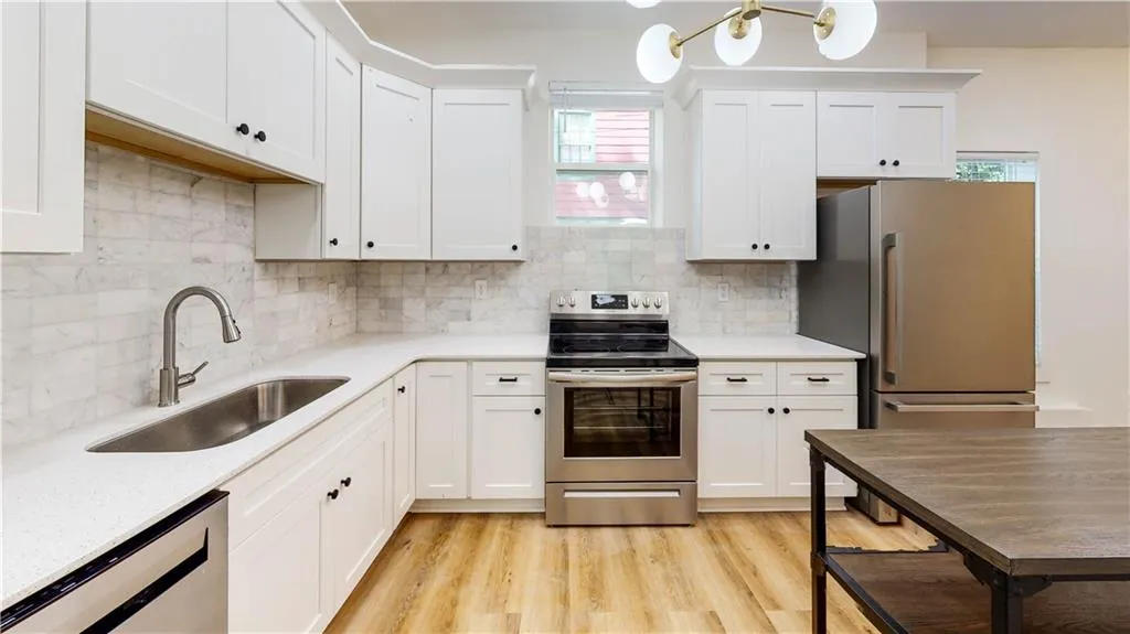 Kitchen with appliances with stainless steel finishes, white cabinetry, light wood-style floors, and backsplash