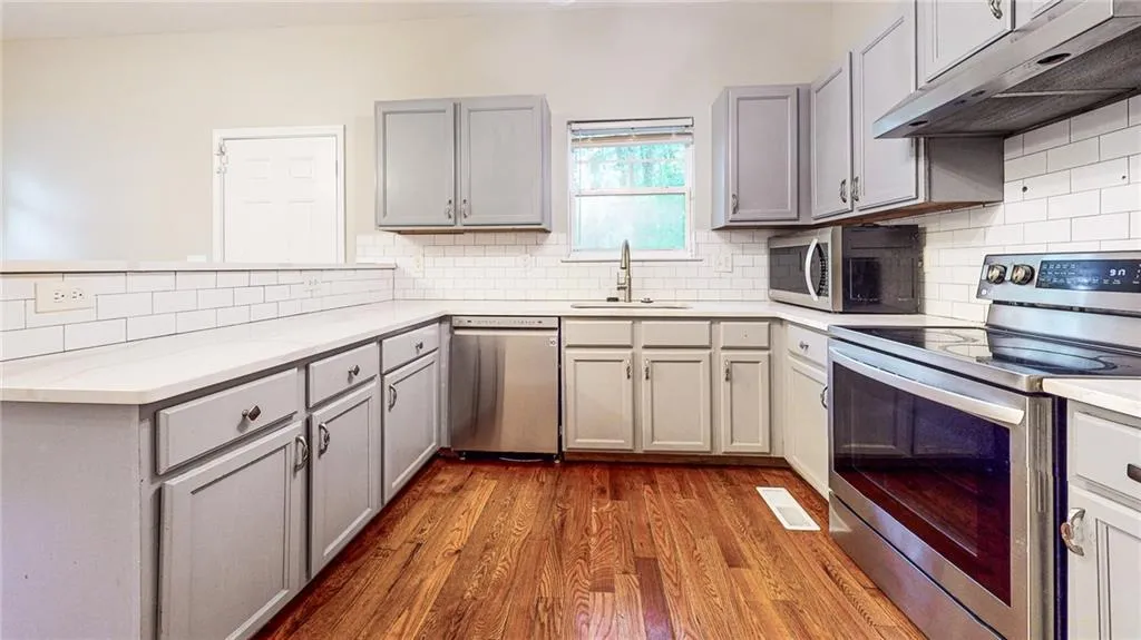 Kitchen featuring stainless steel appliances, under cabinet range hood, gray cabinetry, and dark wood finished floors