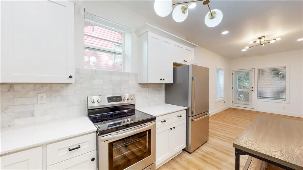 Kitchen with stainless steel appliances, white cabinets, decorative backsplash, light wood finished floors, and a chandelier