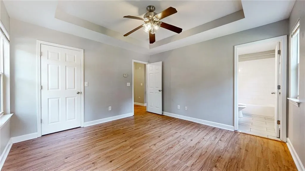Unfurnished bedroom with a tray ceiling, light wood-type flooring, and a ceiling fan