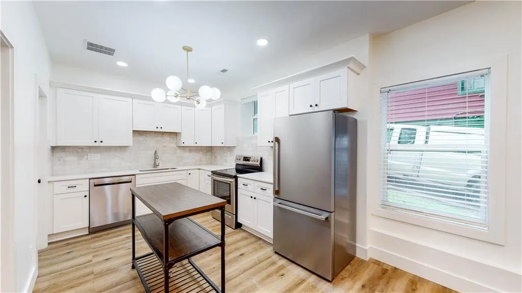Kitchen with stainless steel appliances, a chandelier, pendant lighting, white cabinetry, and light wood-type flooring