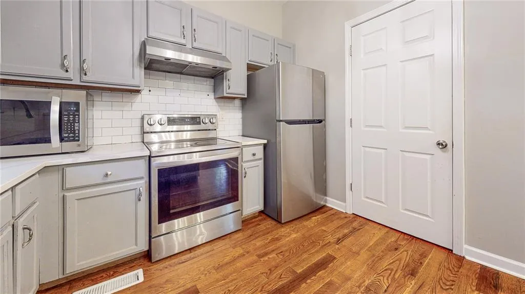 Kitchen with appliances with stainless steel finishes, light countertops, under cabinet range hood, decorative backsplash, and light wood-style floors