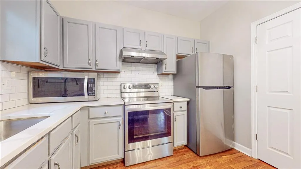 Kitchen with appliances with stainless steel finishes, light wood-style flooring, backsplash, under cabinet range hood, and light stone countertops