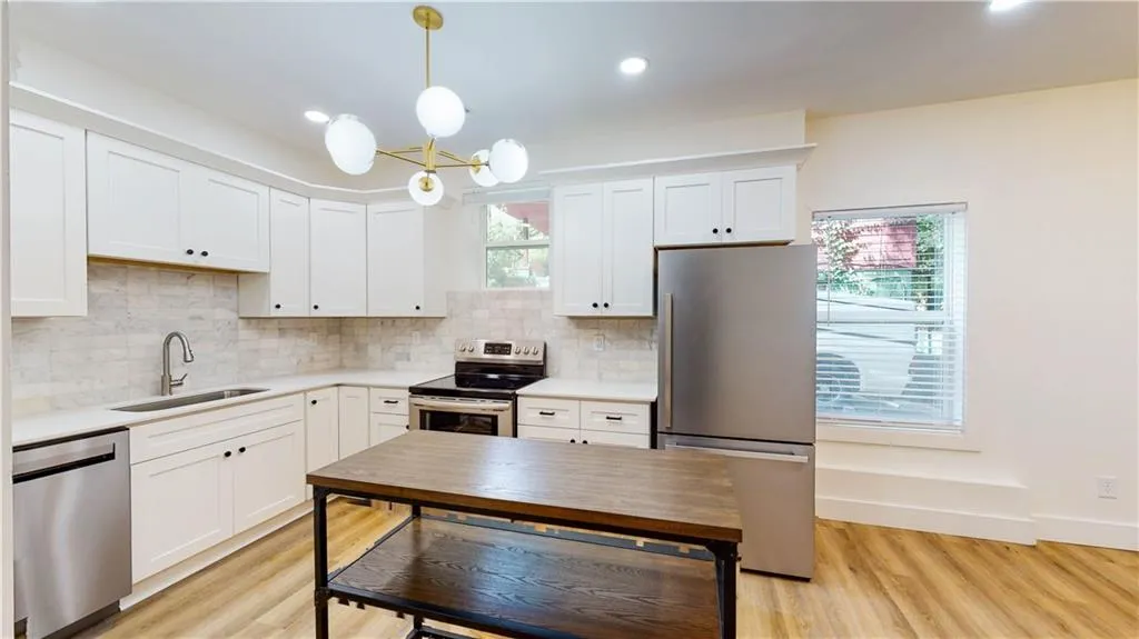 Kitchen with stainless steel appliances, white cabinets, hanging light fixtures, backsplash, and light wood-type flooring