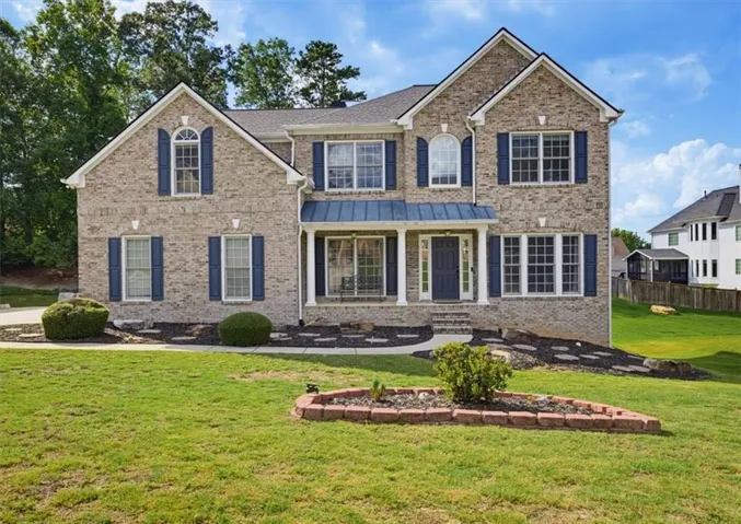 Two-story brick exterior featuring a covered front porch with white columns, blue metal awning, dark blue front door, and matching blue window shutters