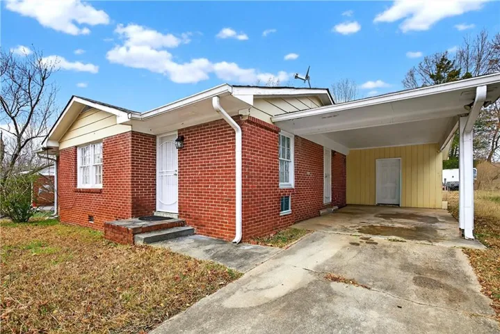View of front of house with brick siding, concrete driveway, a carport, and crawl space