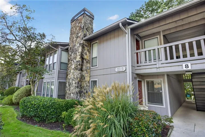 Exterior building featuring gray horizontal siding, a prominent stone chimney, private balconies with wood railings, and manicured landscaping