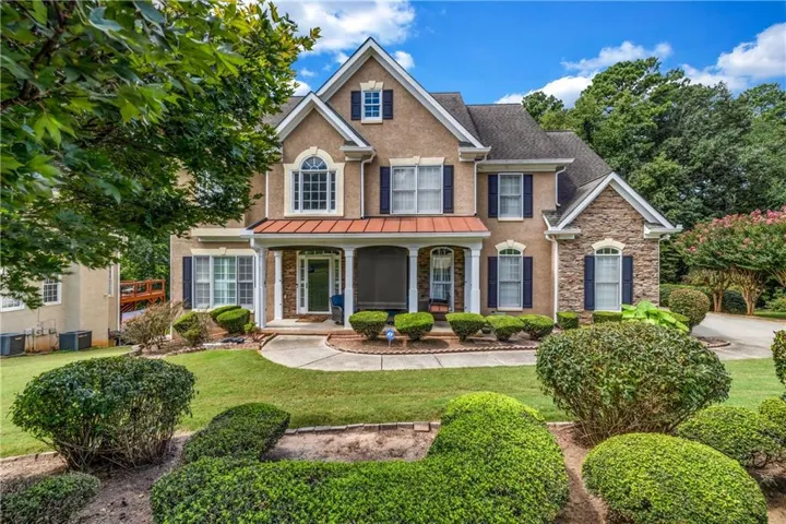 Traditional-style residence featuring a stucco and stone exterior, dark shutters, an arched window, and a covered front porch with columns