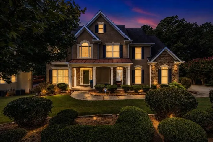 Stately residential exterior featuring a multi-gable roofline, stone veneer accents, a covered front porch with columns, decorative window shutters, and manicured landscaping with pathway lighting