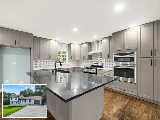 Kitchen featuring an expansive island with a dark countertop, grey shaker cabinetry, stainless steel appliances, a tile backsplash, and wood-finish flooring