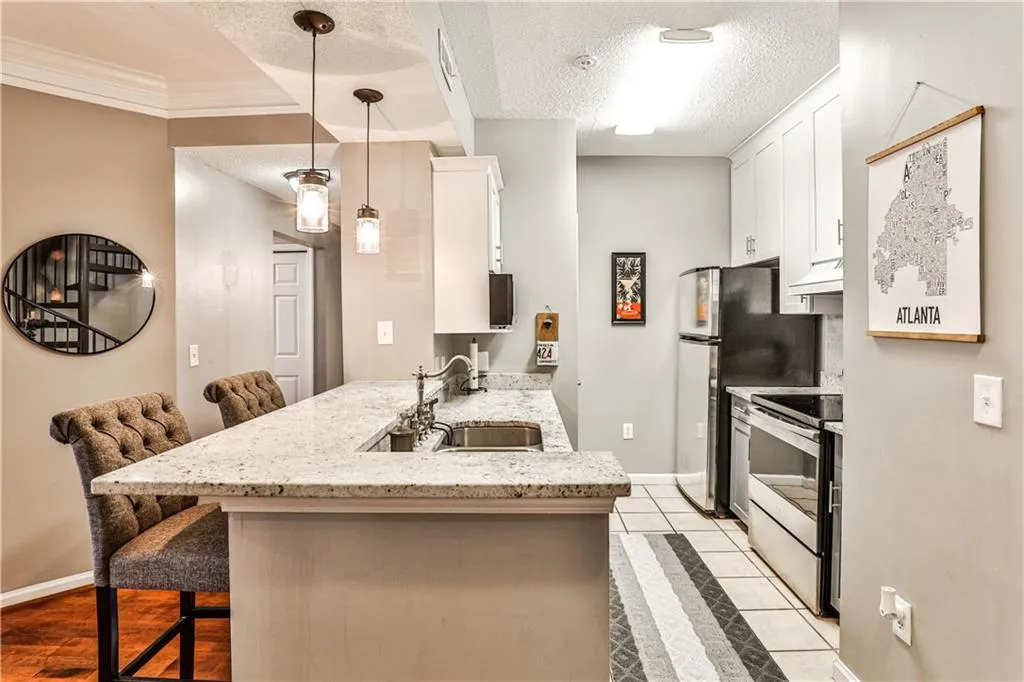 Kitchen featuring stainless steel appliances, under cabinet range hood, a kitchen bar, a sink, and a textured ceiling