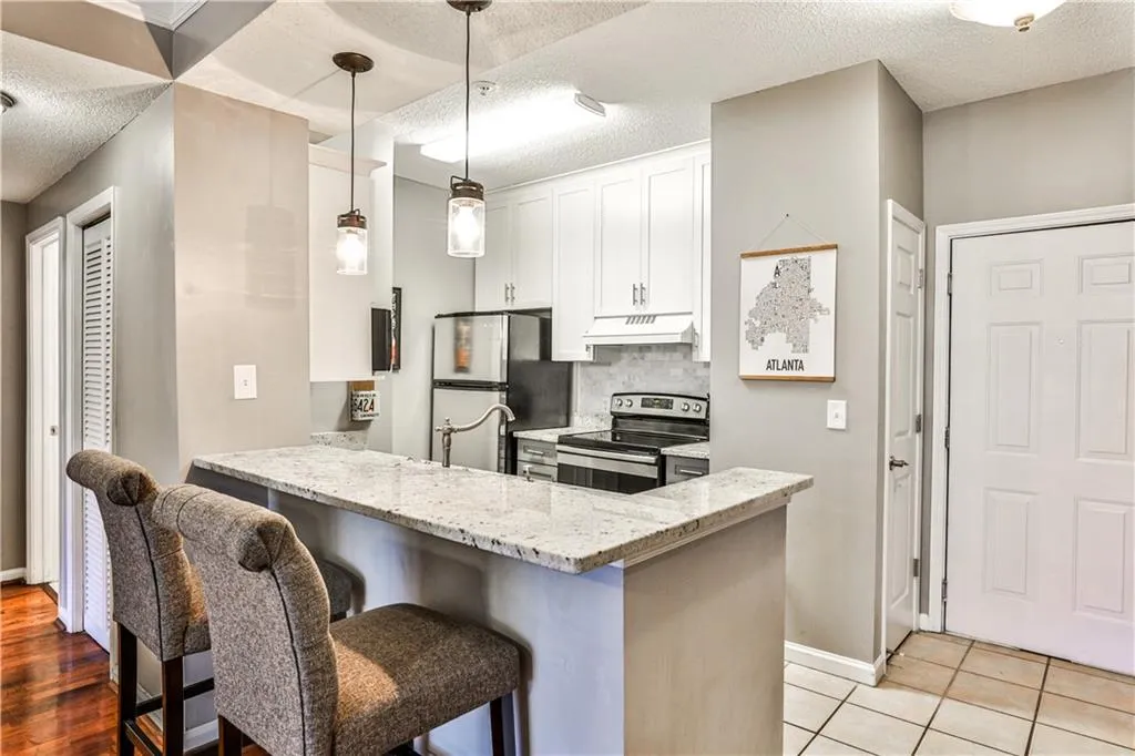 Kitchen featuring light stone countertops, under cabinet range hood, appliances with stainless steel finishes, white cabinetry, and a peninsula