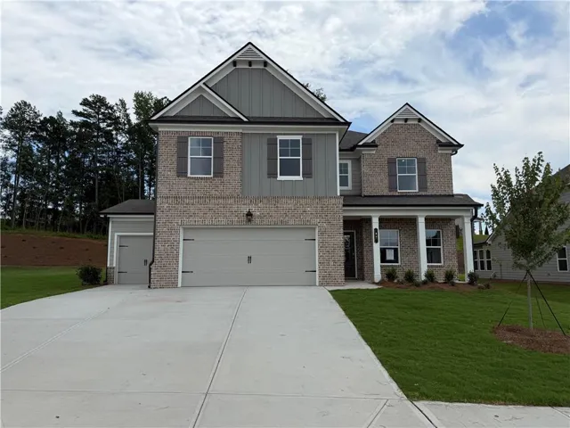 Two-story home featuring a brick and siding facade, a two-car garage, an additional single-car garage, a covered front porch with white columns, and a concrete driveway