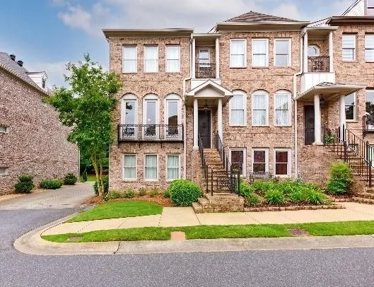Brick facade townhome with covered entry, arched windows, and iron balconies