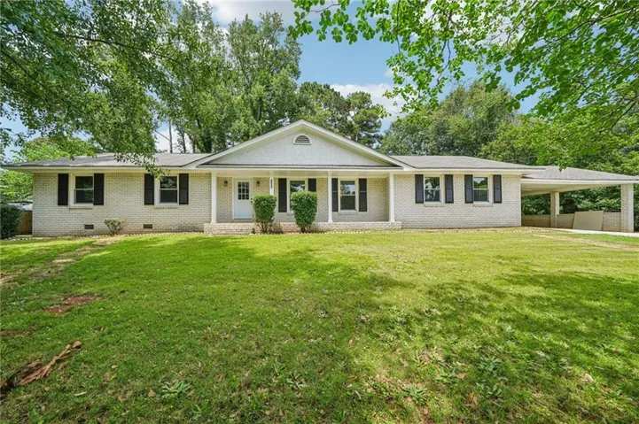 White brick exterior with black shutters, a covered front porch, and a dedicated carport