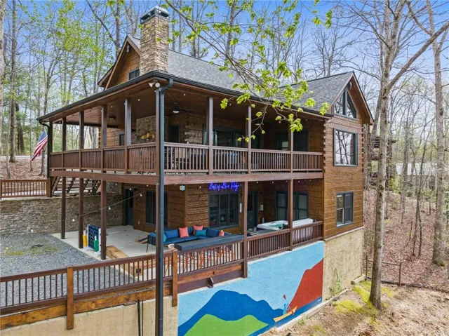 Multi-level wood-sided exterior with stone accents, featuring a prominent stone chimney, multiple covered balconies, and an exposed aggregate patio