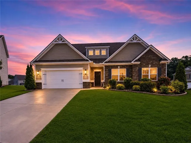 Stone and siding facade featuring a two-car garage, manicured lawn, and mature landscaping