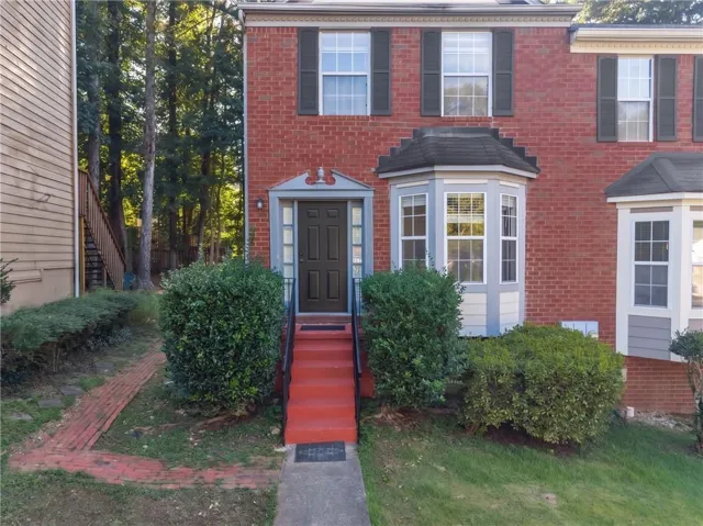 Red brick exterior with dark shutters, bay window with multiple panes, stone door surround, and red-painted entry stairs