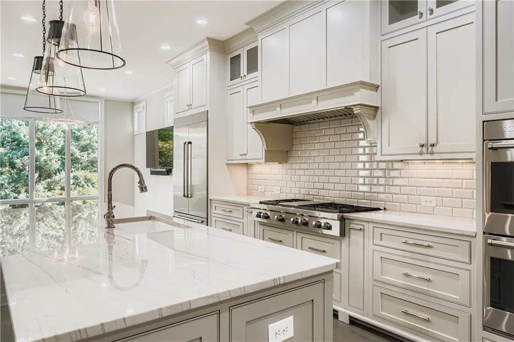 Kitchen featuring appliances with stainless steel finishes, tasteful backsplash, light stone counters, a center island with sink, and glass insert cabinets