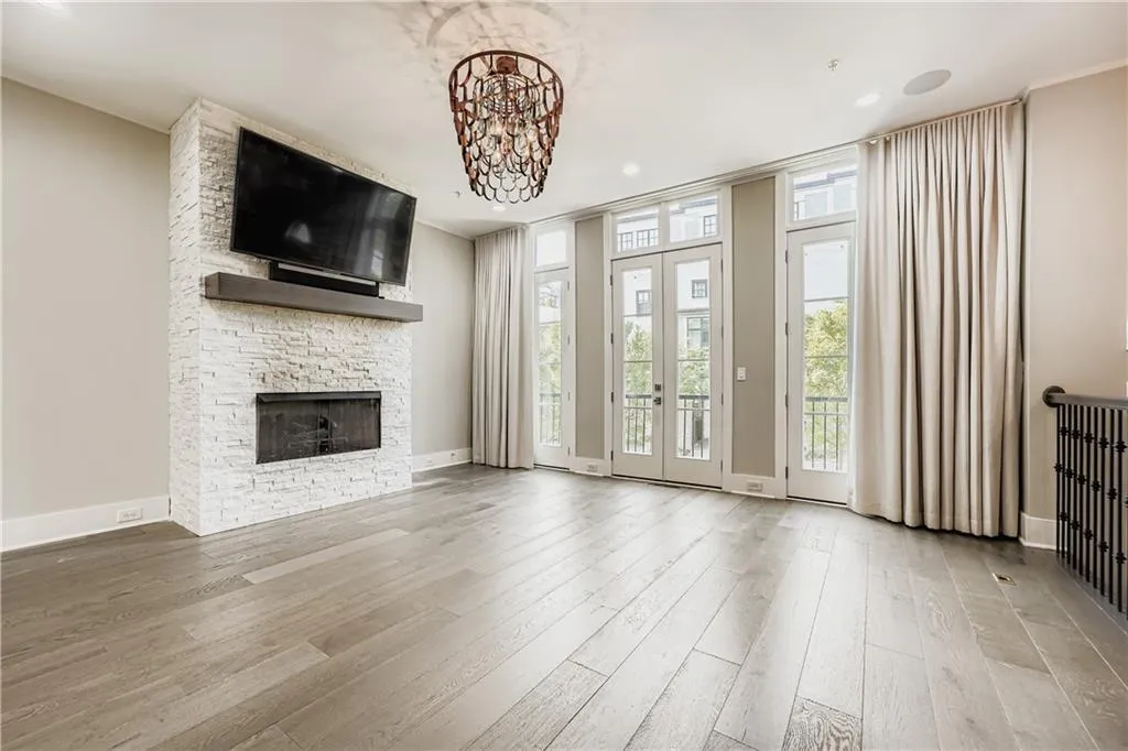 Unfurnished living room featuring wood finished floors, a stone fireplace, and a chandelier