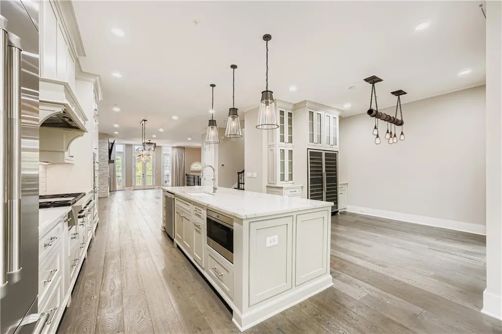 Kitchen featuring beverage cooler, stainless steel appliances, a kitchen island with sink, light wood-style floors, and white cabinets
