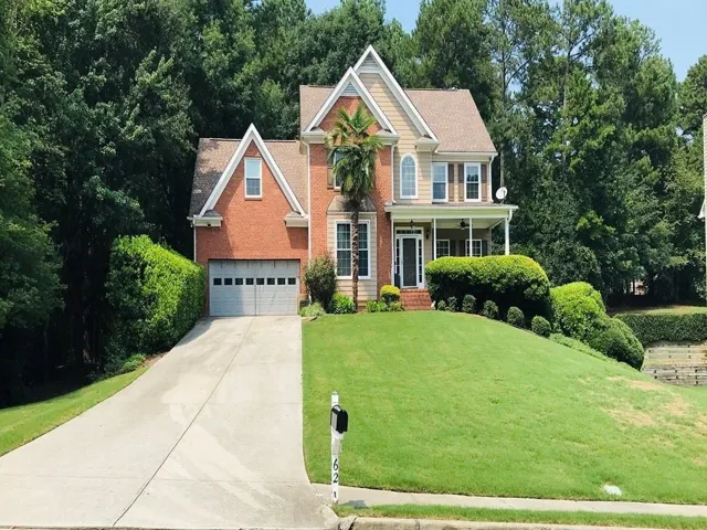 Traditional-style exterior with brick and siding facade, featuring a two-car garage, mature landscaping, an invited covered porch and an attached window detail.
